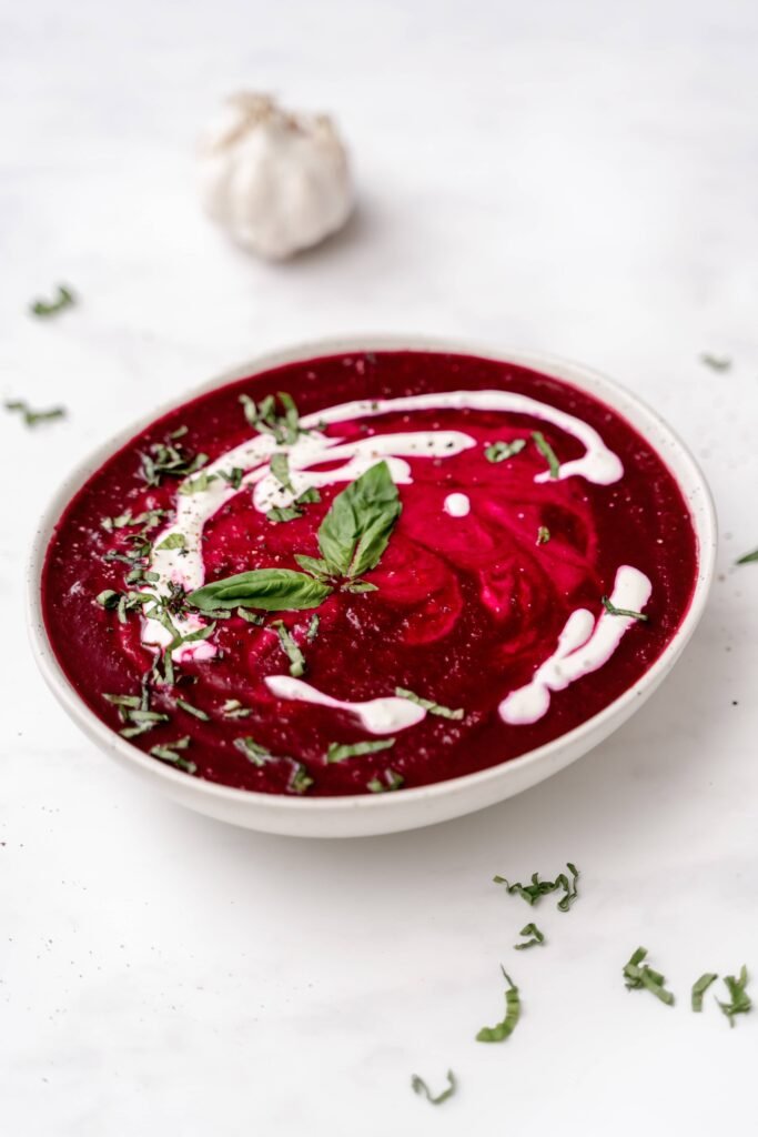 Soupe rouge vif aux betteraves et ail dans un bol avec filet blancs de yogourt nature et parsemée de feuilles de basilic frais