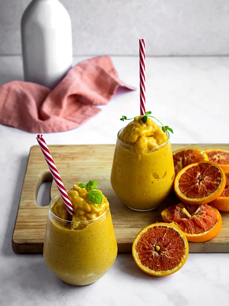 2 verres débordants de smoothie glacés jaunes à la mangue avec tranches d'oranges