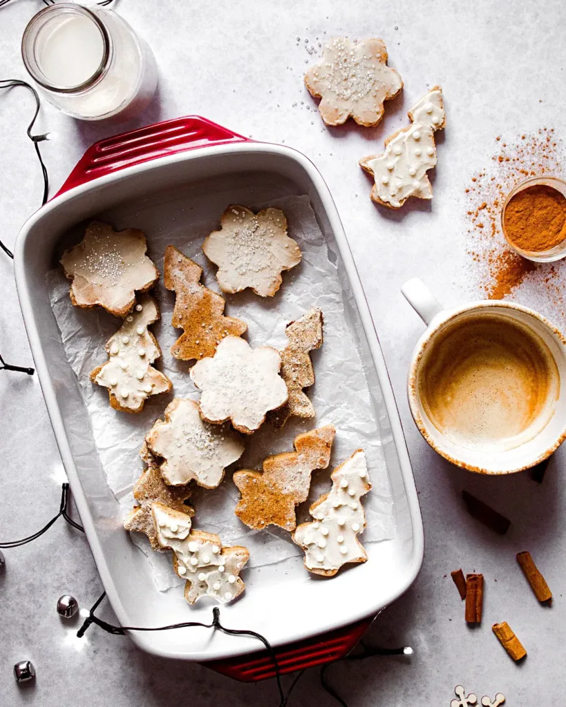 Plat rempli de biscuits en formes de flocons et de sapins décorés pour Noël avec une tasse de café
