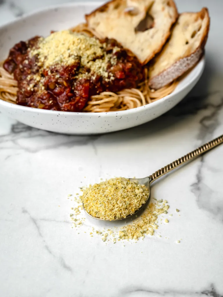 cuillère de parmesan vegan avec bol de spaghetti bolognaise